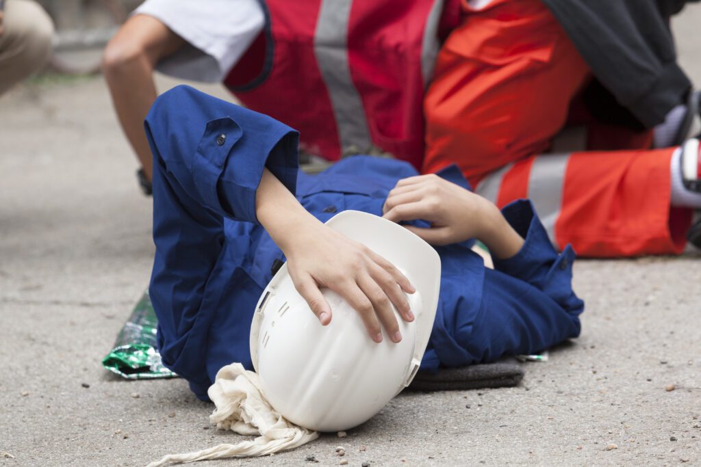 Construction worker in a hard hat is on the ground after falling