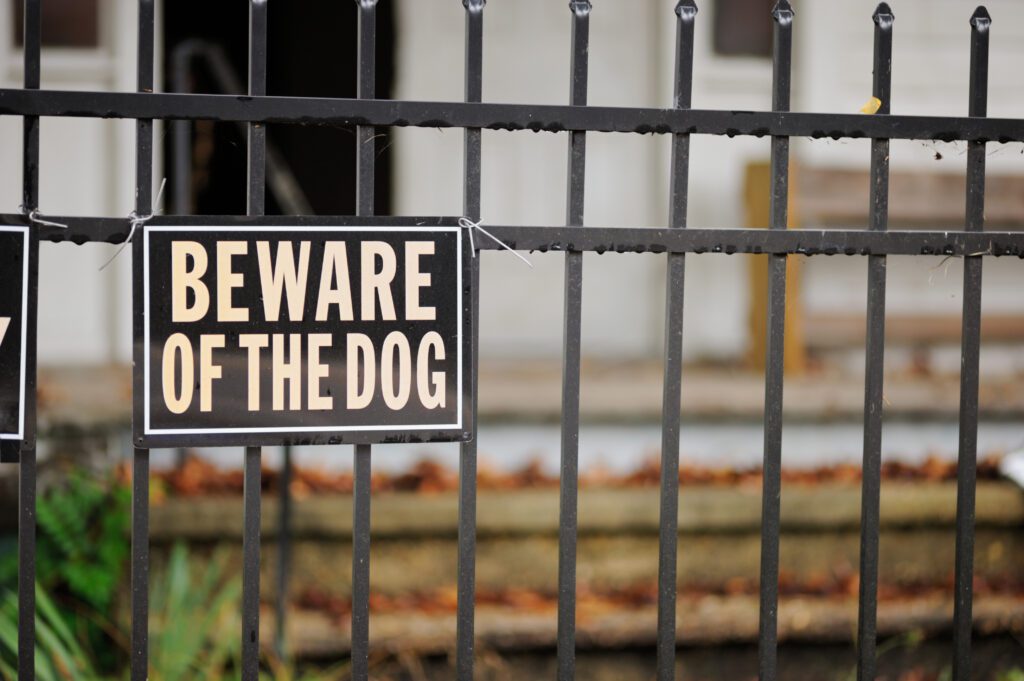 Close up of beware of the dog sign on metal fence in front of unrecognizable house