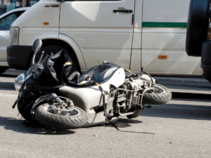 Motorcycle on its side in the middle of the road by a car.